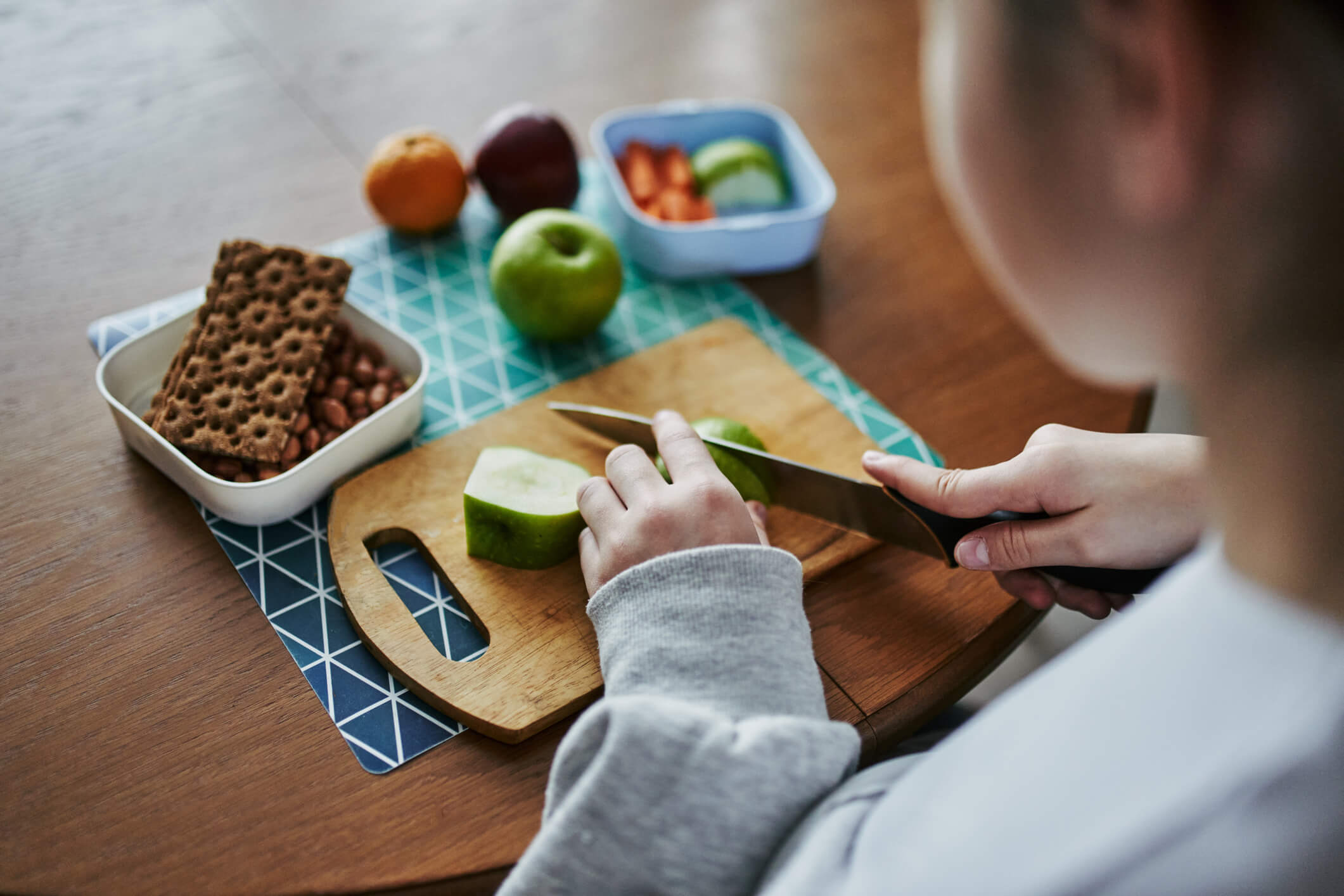 A child using a chopping board to cut up an apple for her school packed lunch.