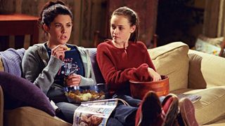 A mother and daughter eat snacks on a sofa