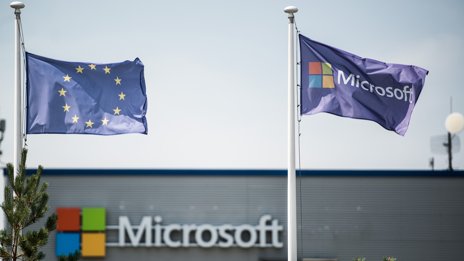 A European Union (EU) flag, left, flies beside a Microsoft flag outside the Nokia Oyj mobile handset factory, operated by Microsoft Corp., in Komarom, Hungary, on Monday, July 21, 2014.