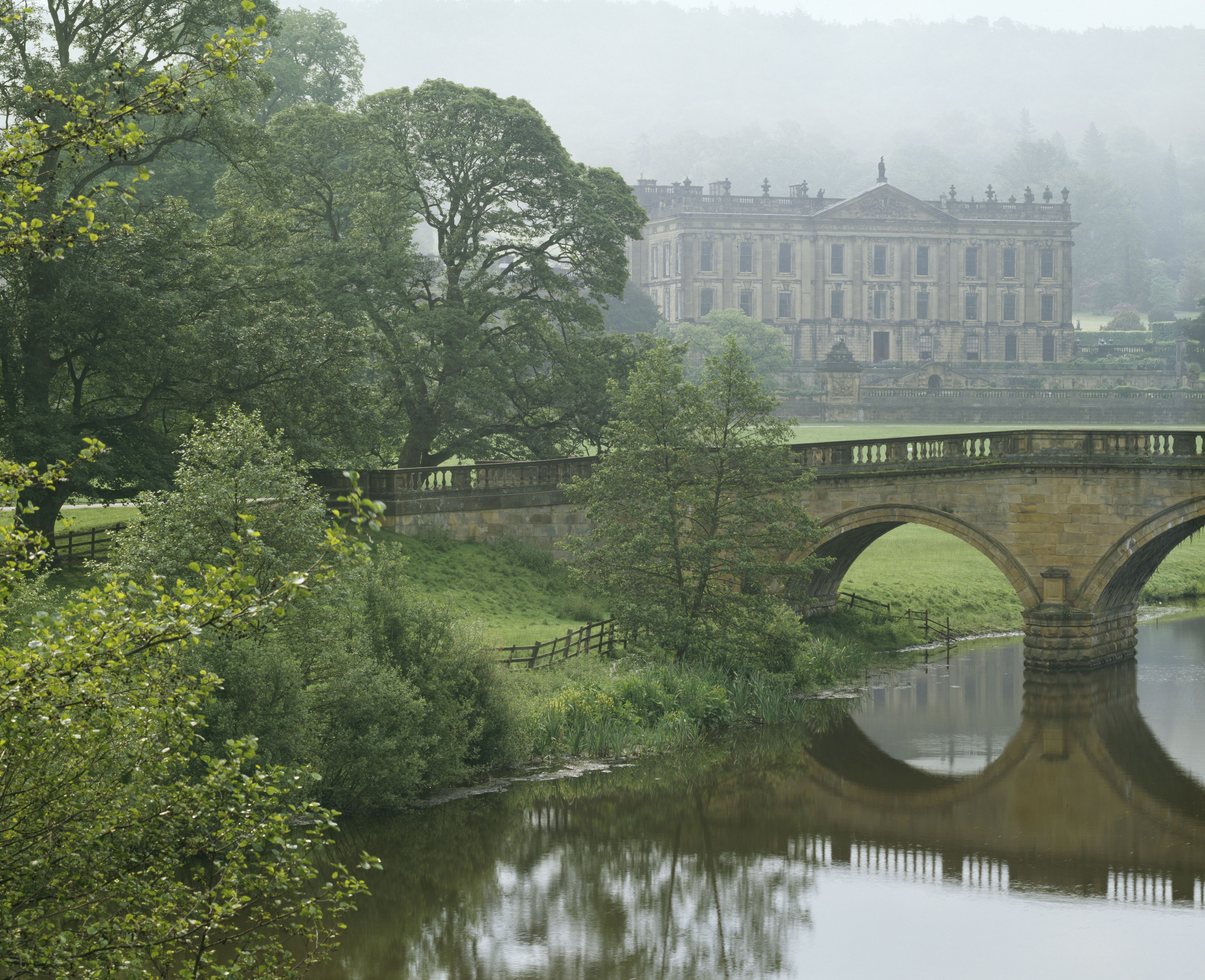 Chatsworth viewed across a stone arch bridge, veiled in fog