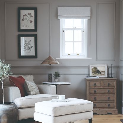 A grey living room with panelled walls and an ivory armchair with a matching footstool