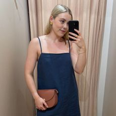 Woman wears blue shift dress, gold jewellery and pink handbag.