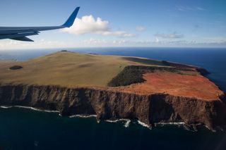 An aerial view of Easter Island and the surrounding Pacific Ocean with the plane's wing in the left corner