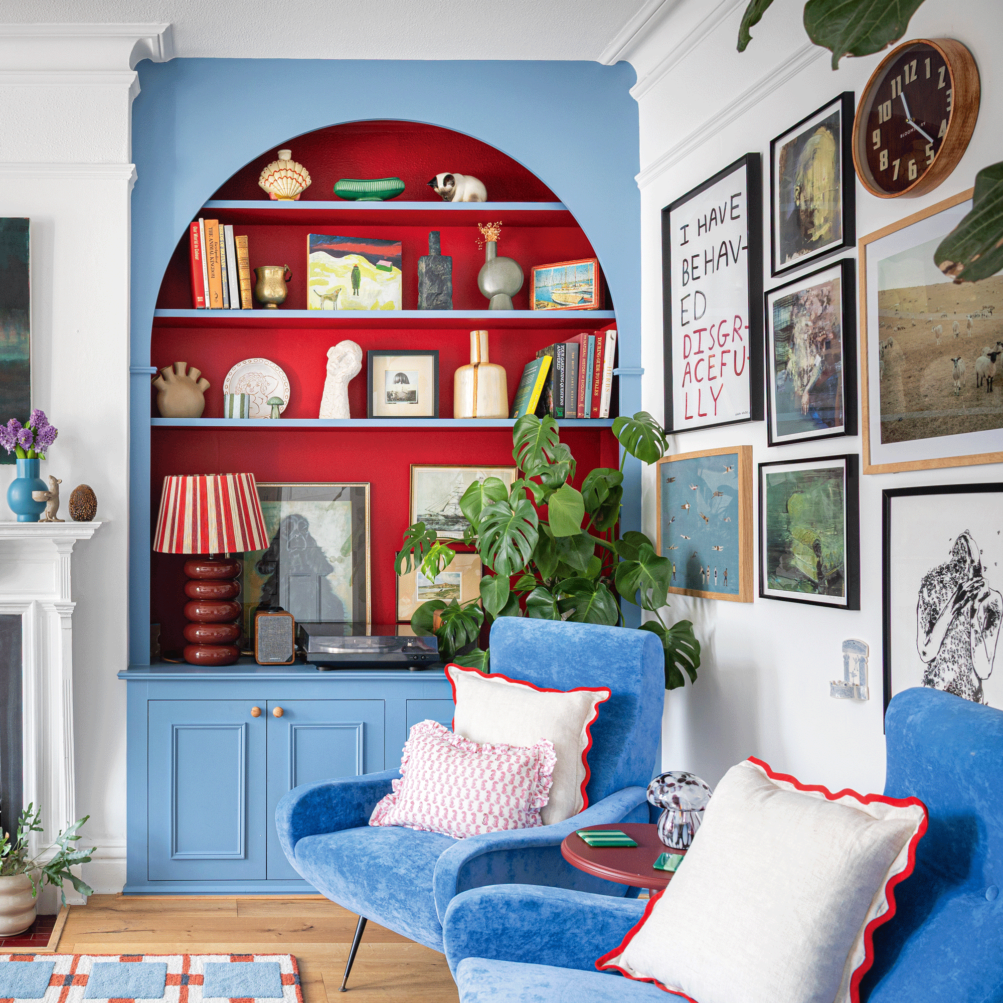 a living room with bright blue painted alcove shelving with bold contrasting red recessed shelves with a gallery wall and plenty of colour