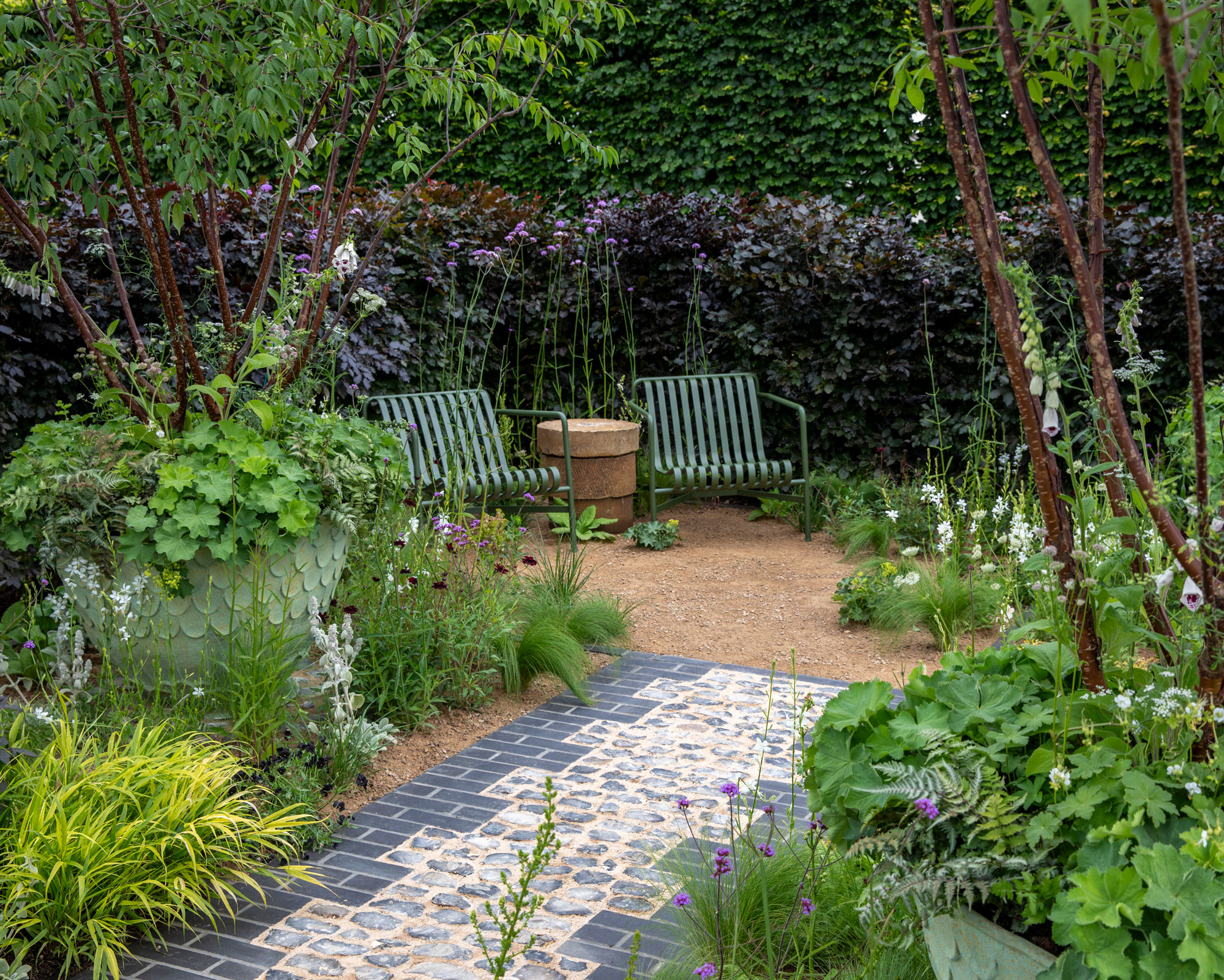 border design with large containers planted with small multi-stem trees, paved design, gravel landscaping, garden chairs and beech hedge