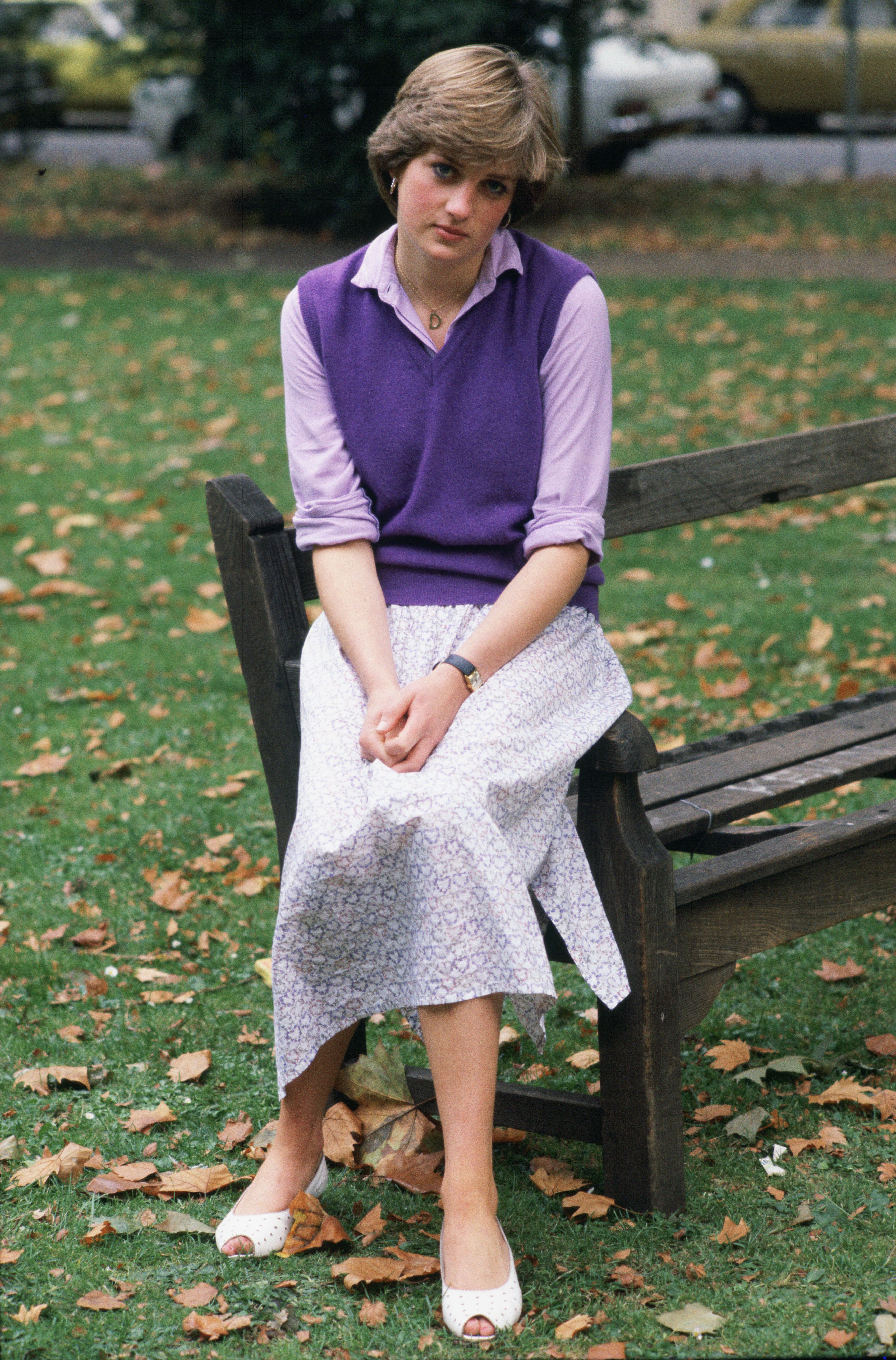 Princess Diana sitting on a park bench in a purple vest and skirt