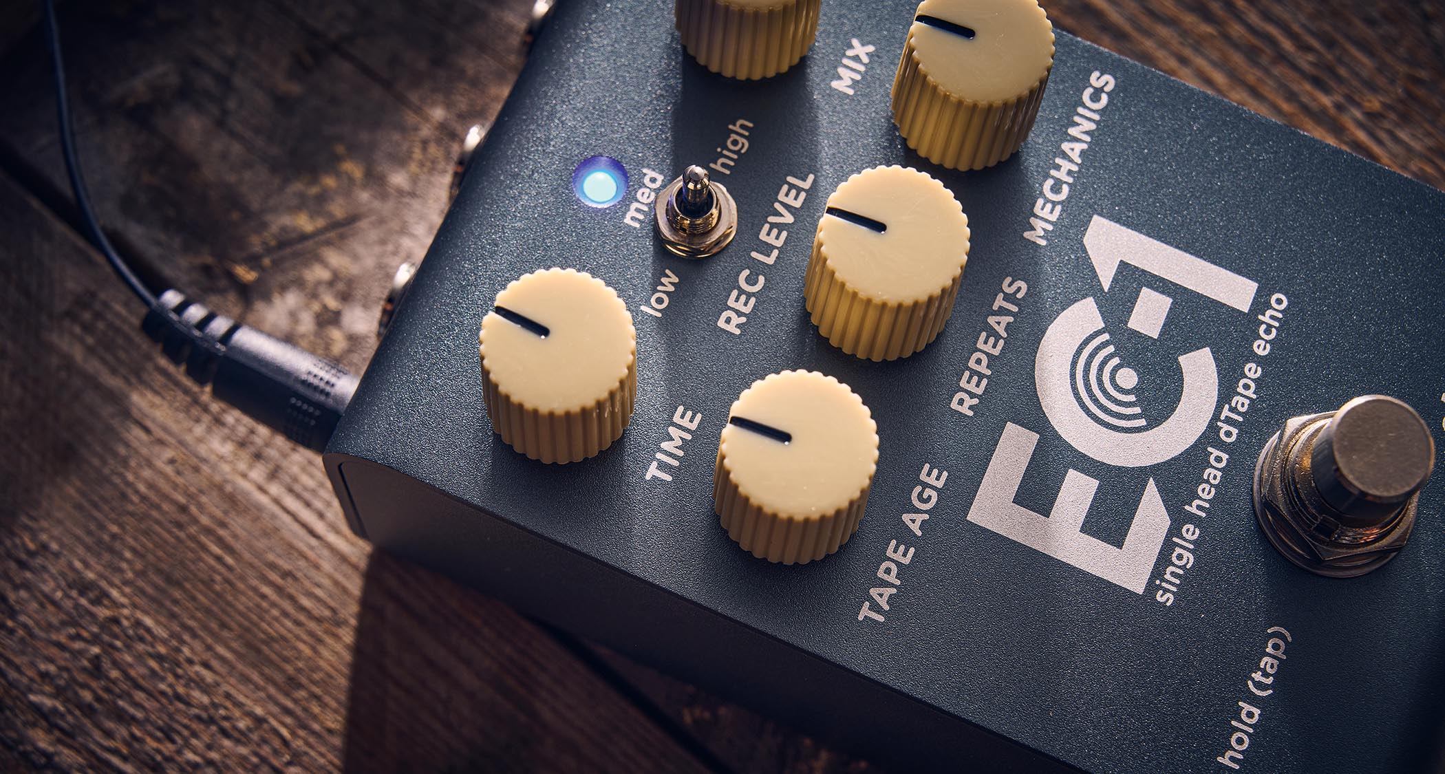 Strymon EC-1 Single Head dTape Echo: the metallic gray box has cream dials, an LED that lights up blue and/or red, and is photographed here against a wooden background.