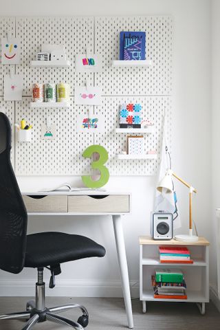 Corner of a home office with white desk, white pegboard and black desk chair