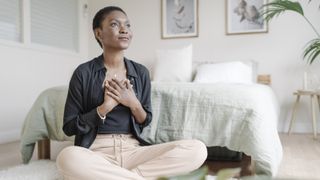 woman with hand on chest showing gratitude while praying sitting on the floor in her bedroom