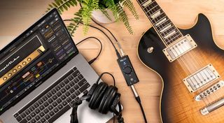 The iRig HD X guitar interface next to a guitar and a MacBook on a wooden table.