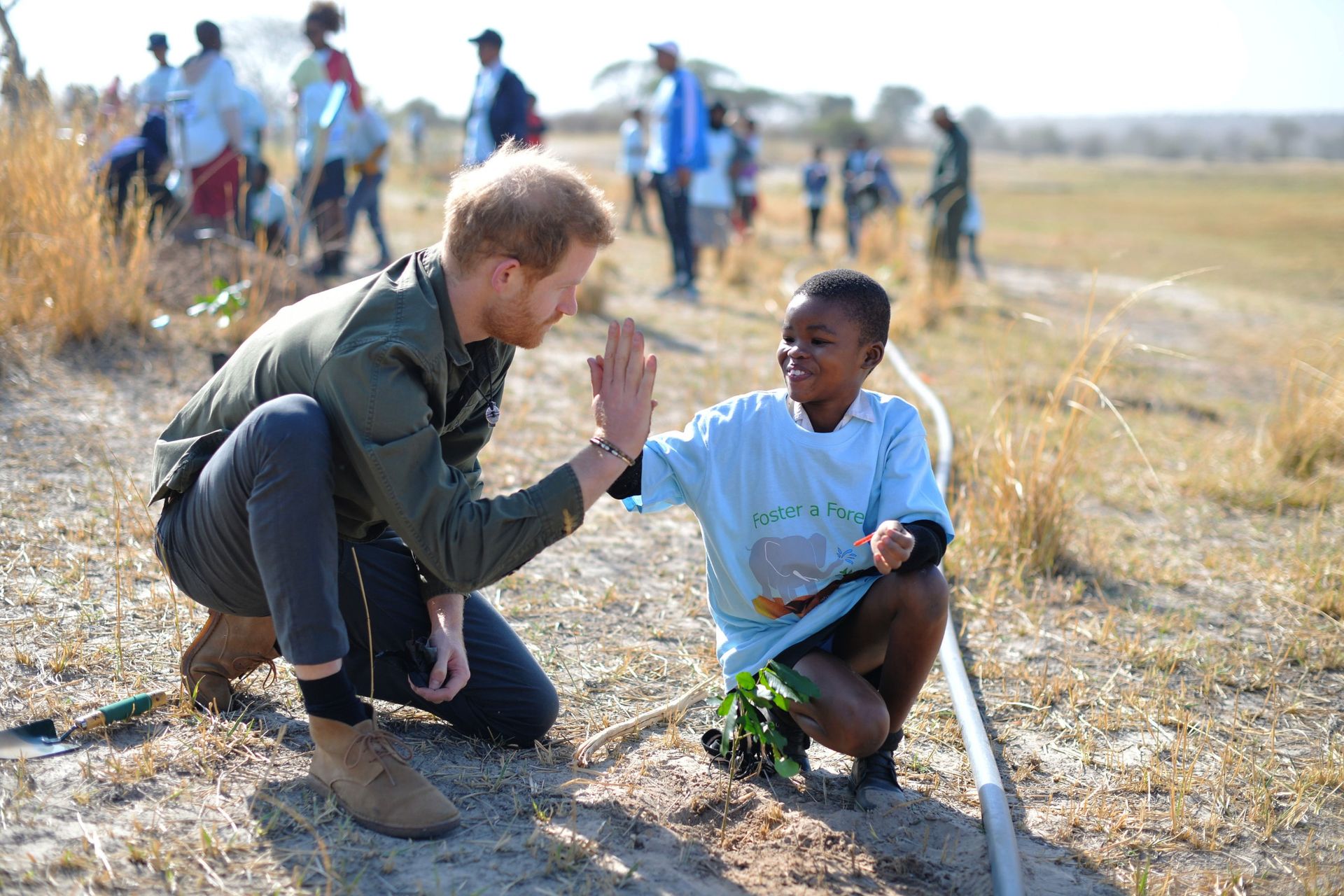 Prince Harry high fiving a boy on the ground in Botswana