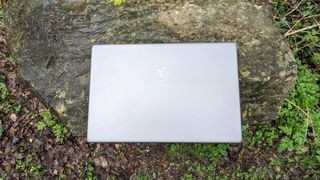 A silver MSI Creator Z17 sitting on a stone bench in a forest setting