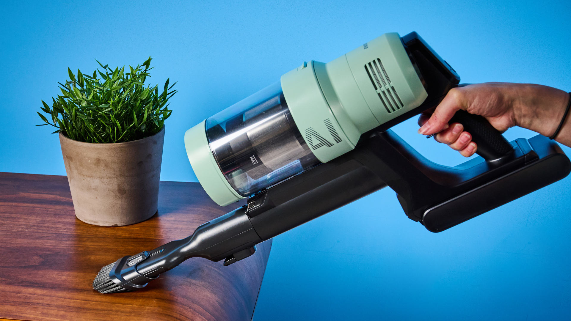 the samsung bespoke jet AI vacuum cleaner in mint green against a blue background, showing its ability to clean carpets and baseboards, as both a stick and a handheld