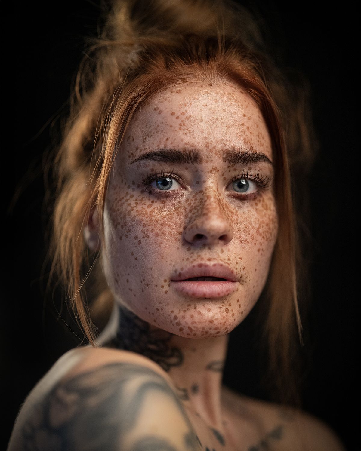 A close-up of a woman with intricate tattoos on their shoulder and neck, highlighted against a dark background
