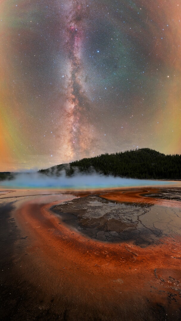 A night sky image shows the streak of glowing Milky Way galaxy above a rust-covered lake.