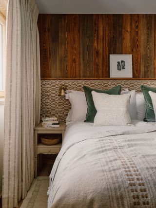 Chalet bedroom with wood paneling, upholstered headboard and wall lights with neutral curtains and linen bedding