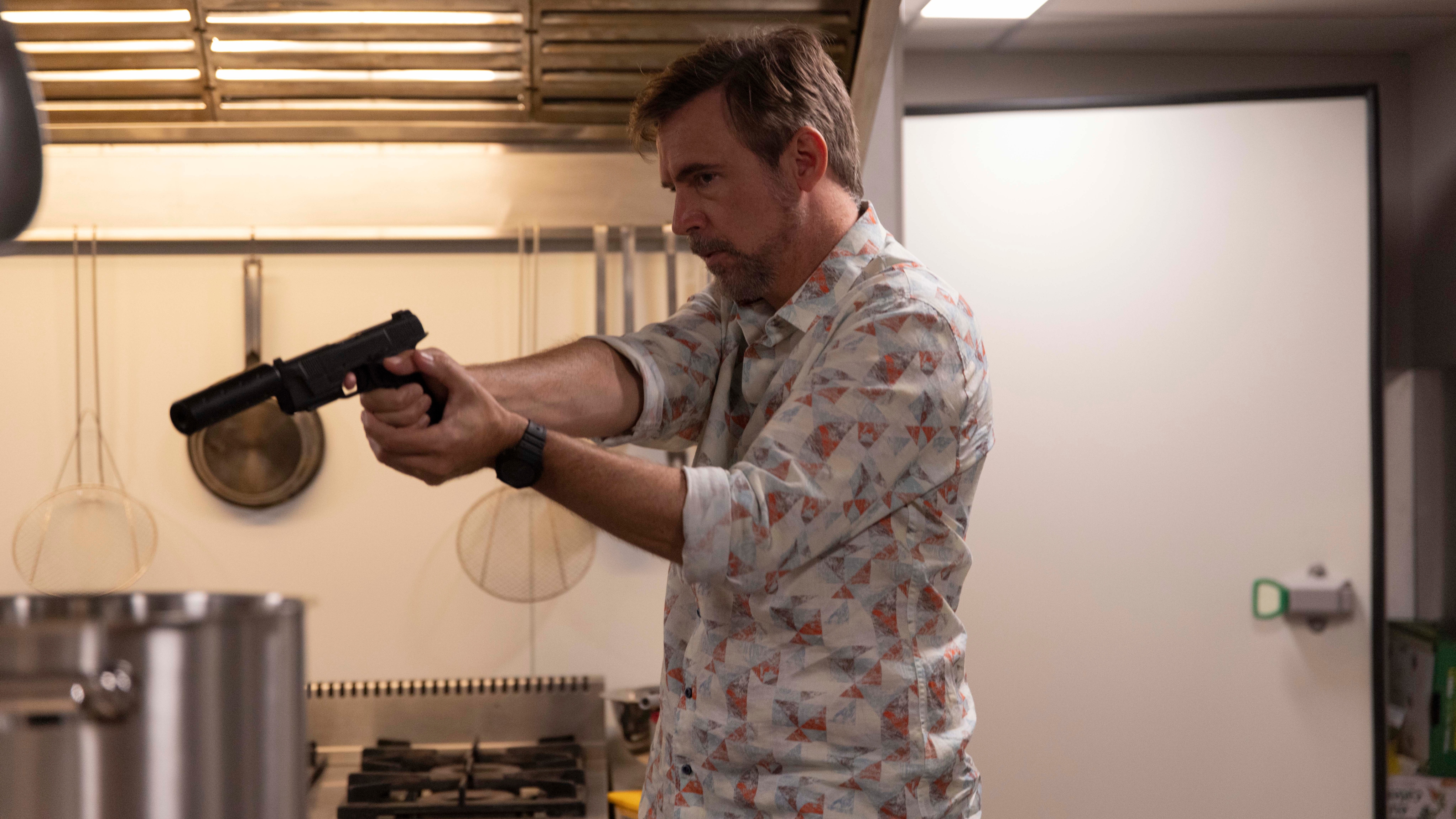 Sean holding up a gun in a kitchen in The Assassin