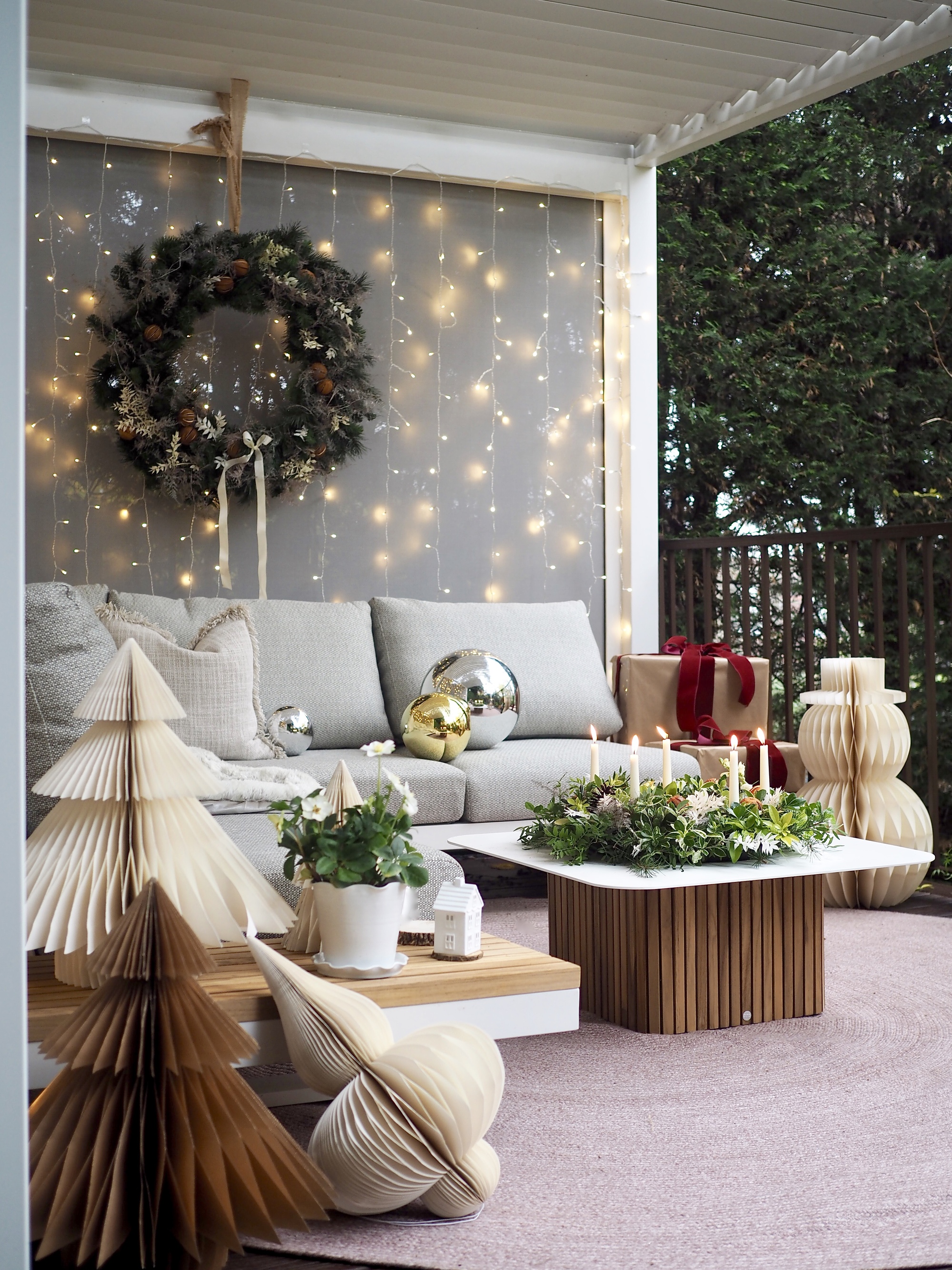A porch decorated for Christmas with a wreath, paper trees, and string lights