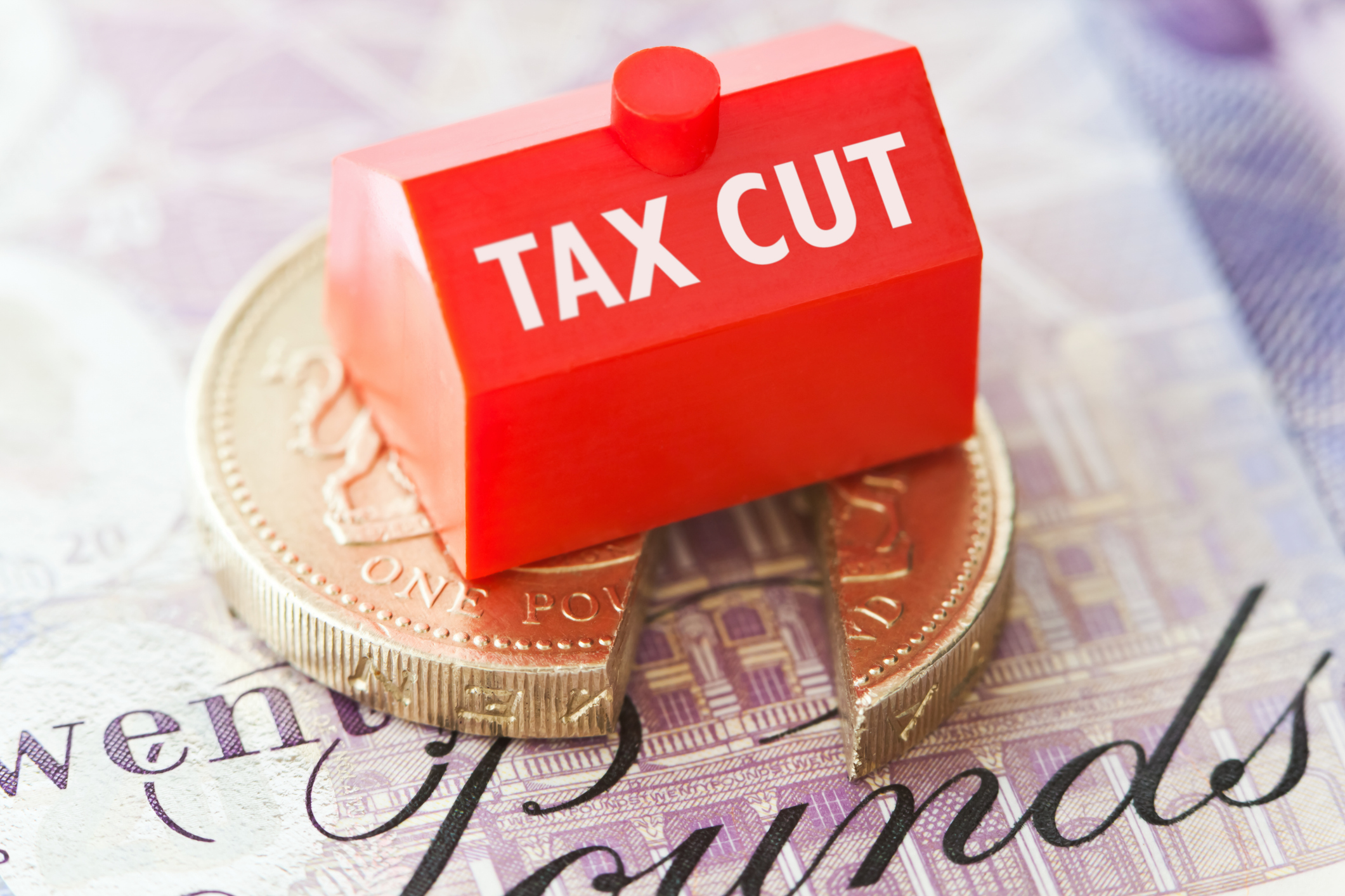 Pound coin cut in half with a block saying tax cut on it