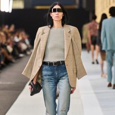 On the S/S 26 Margiela Runway a model wears washed out jeans, tan blazer, beige shirt and a black belt.