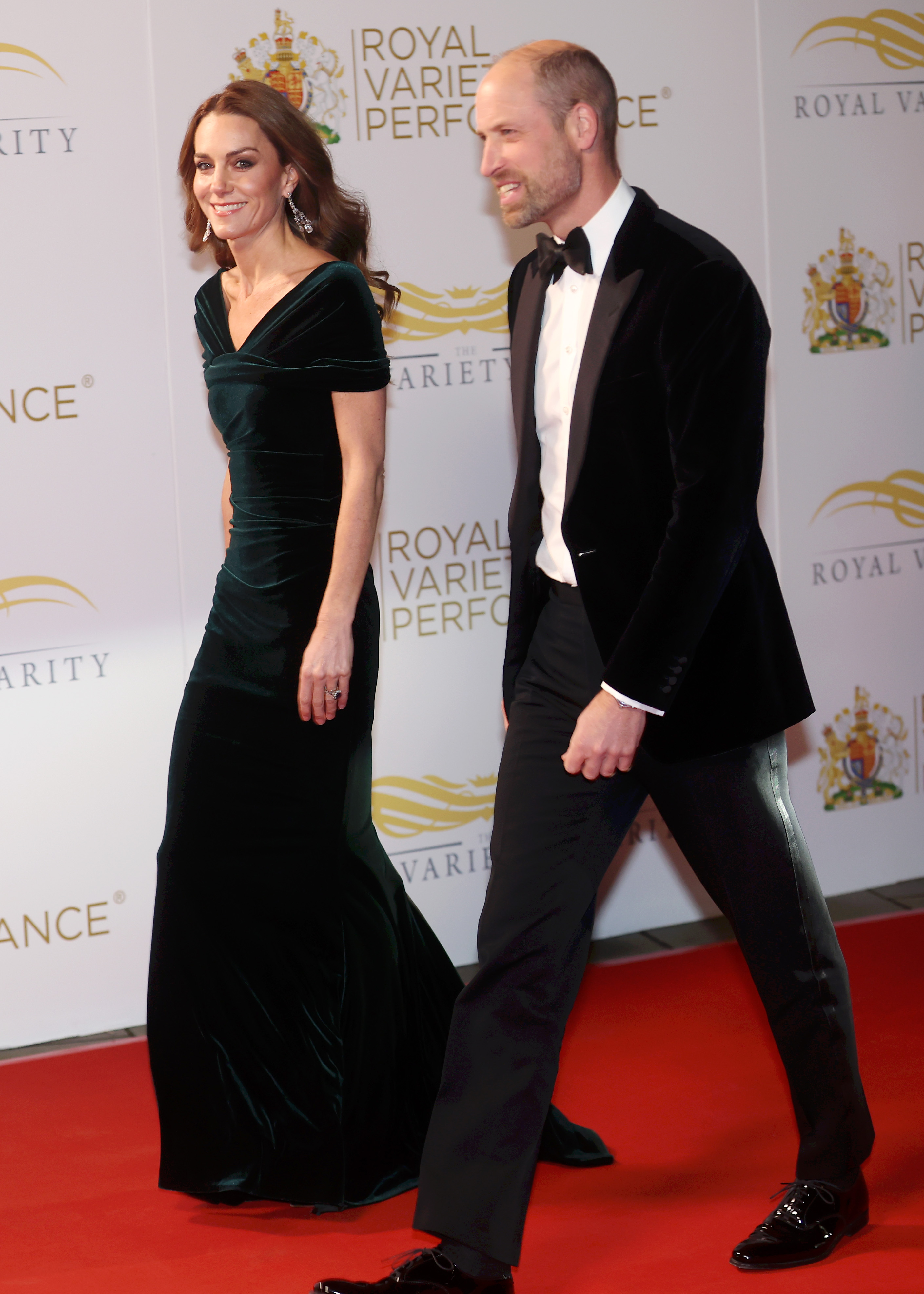 Kate Middleton wearing a velvet gown walking a red carpet next to Prince William