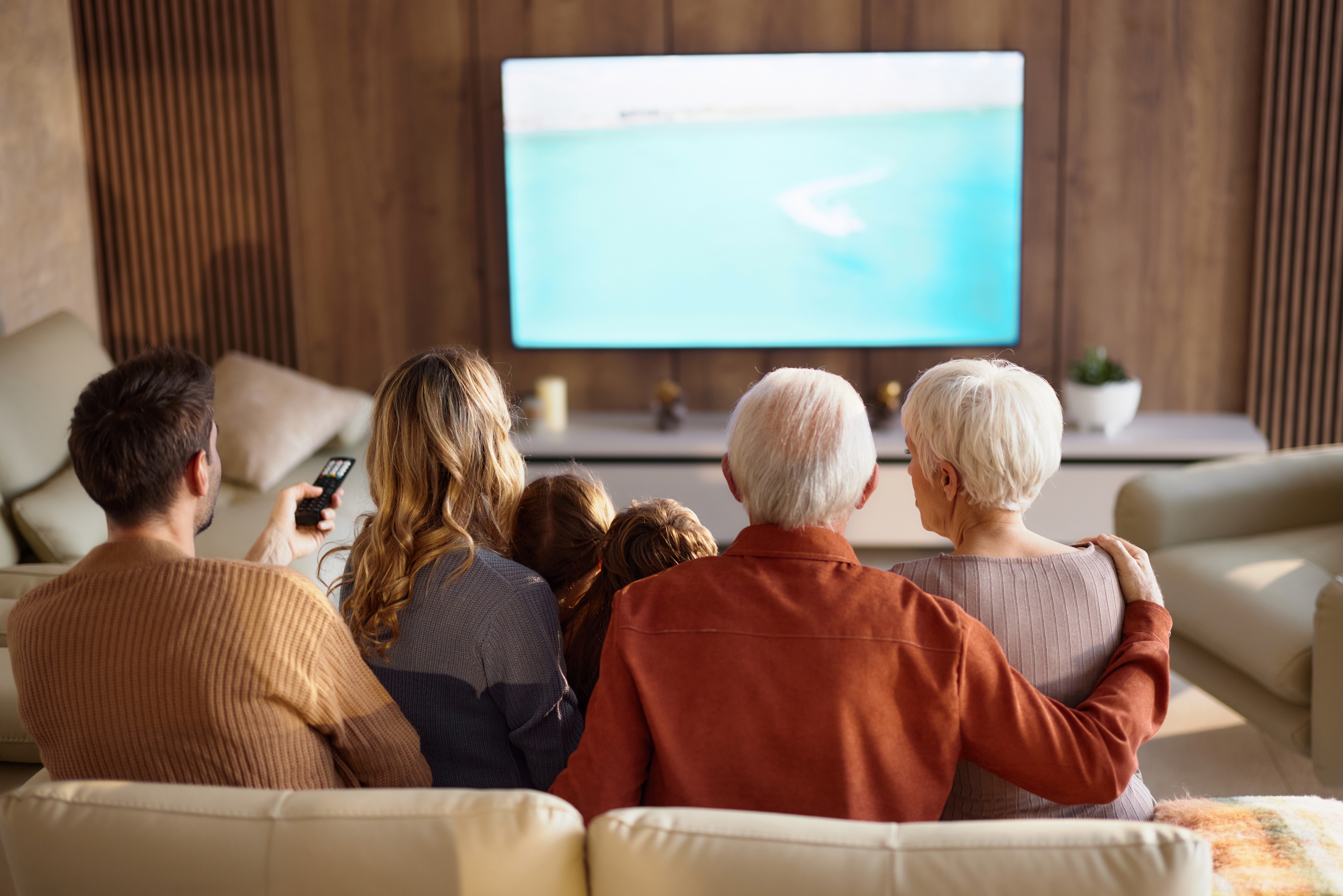 Three generations of a family sitting on couch, watching streaming services on tv.