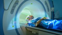 white woman in a blue surgical gown laying down as she's sliding into an MRI scanner