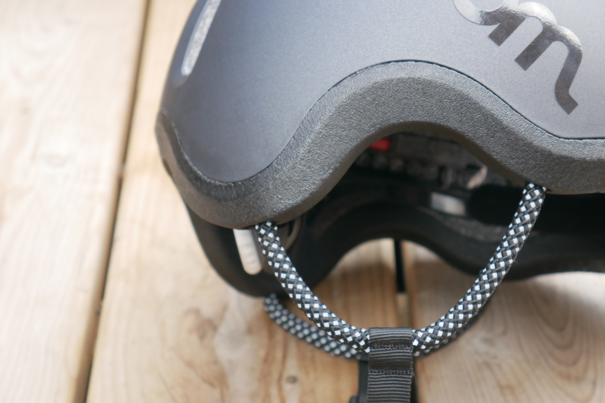 side view of the Woom Ready Kids Bike Helmet straps in black against a backdrop of a wooden deck