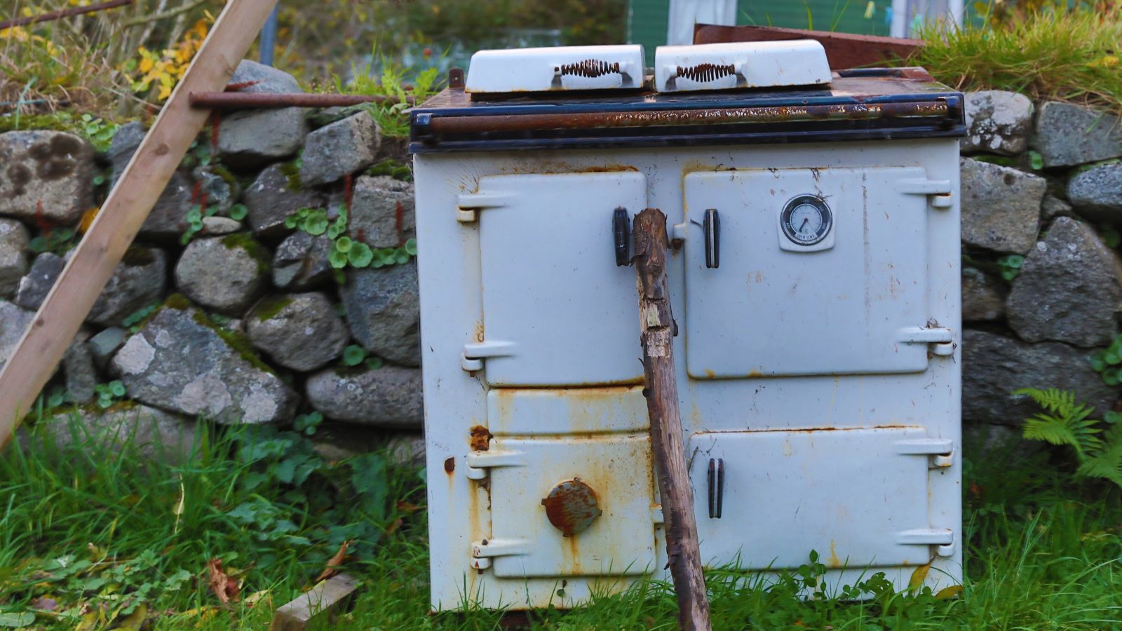 Derelict aga cooker dumped in a field with timber propping up the door.