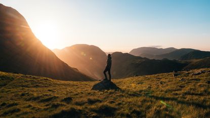 Best walking trousers: a man stands in the middle of a field looking up at sun dappled mountains