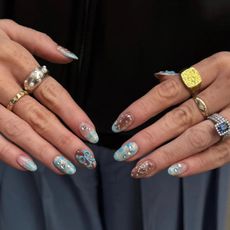A picture of a woman's hands wearing lots of rings with blue and brown nail art