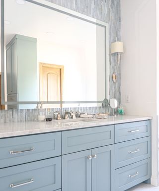 A light blue bathroom with a large mirror and stone countertop