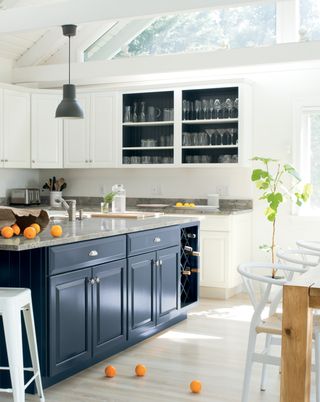 A kitchen with a blue island, white walls and white cabinetry with glass doors. Light wooden-effect flooring