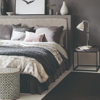 Dark grey walls behind double bed with dark grey pillows and throw blankets