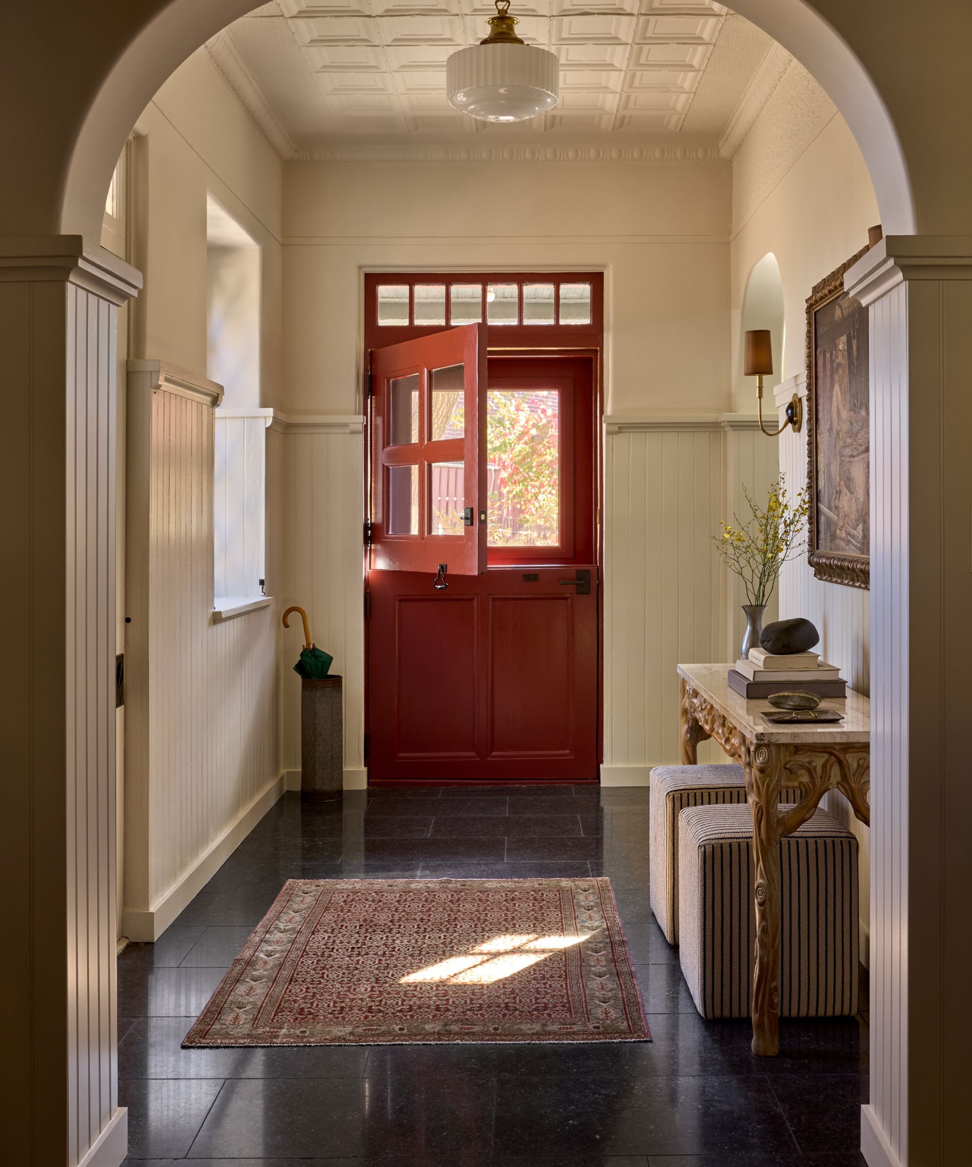 Cream entryway with dark red door and carved wooden console table
