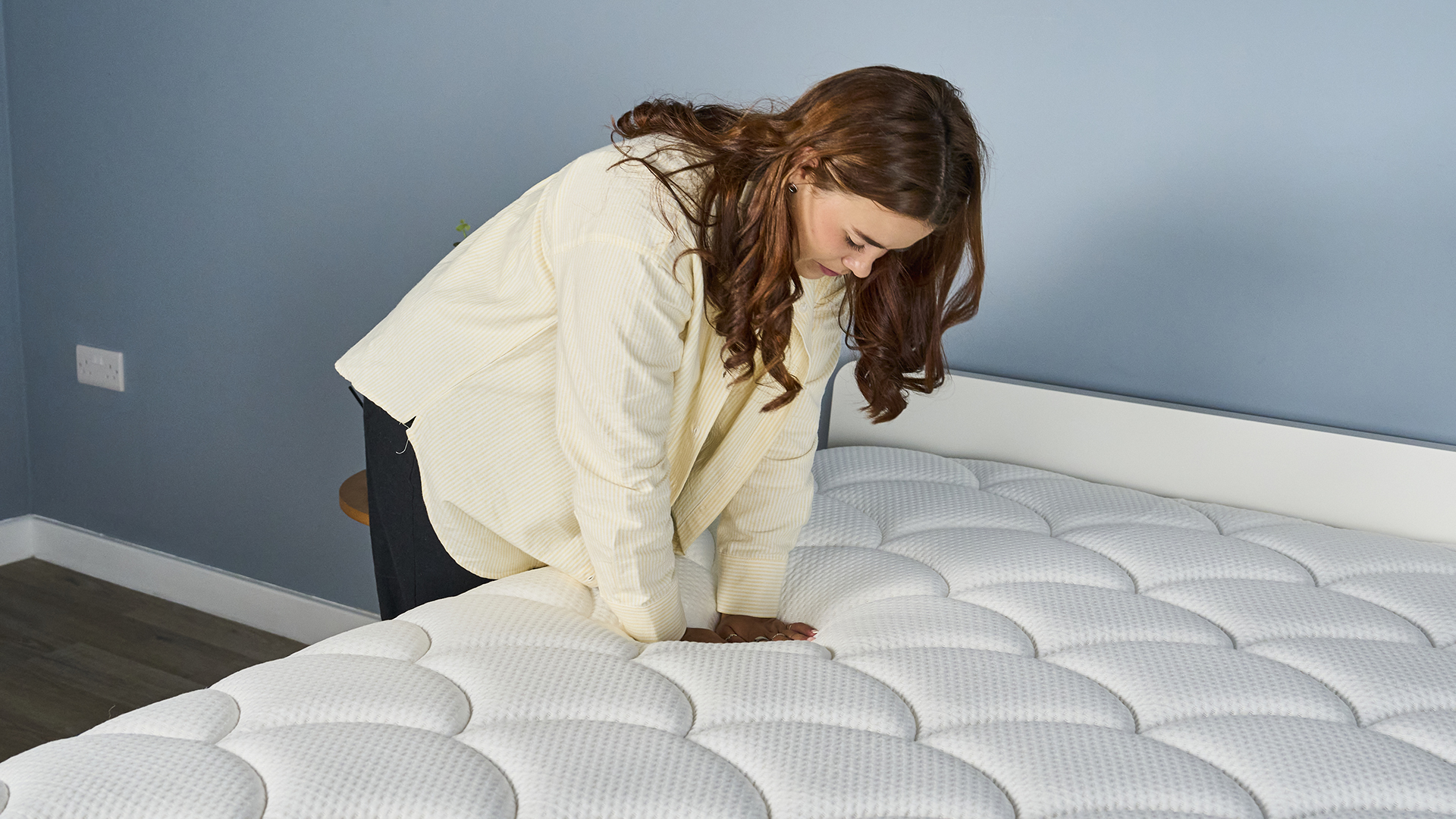 A Tom&#039;s Guide Tester wearing a yellow cardigan pressing down on the DreamCloud Classic mattress to determine how firm it feels