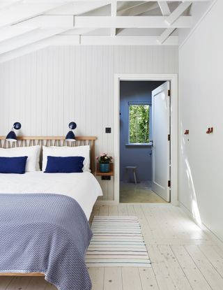 A blue and white cabin bedroom with light wood flooring, shiplap wall paneling and blue wall lights above bed