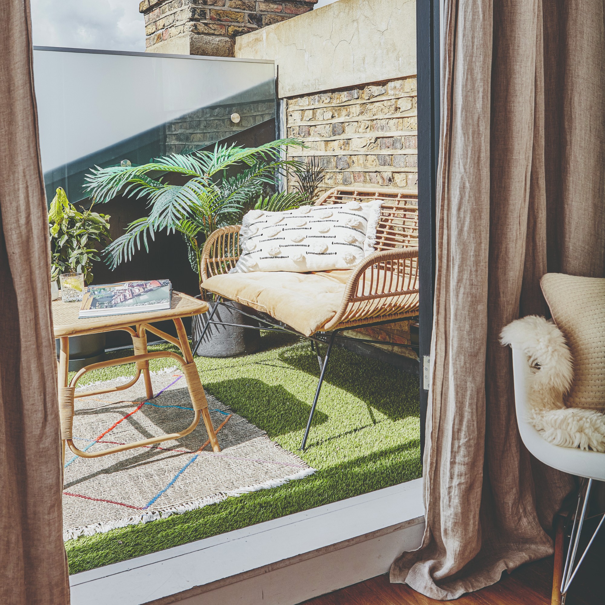 A balcony with a rattan two-seater outdoor sofa and a bamboo coffee table surrounded by potted plants