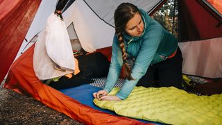 A woman in a tent is deflating a yellow sleeping pad