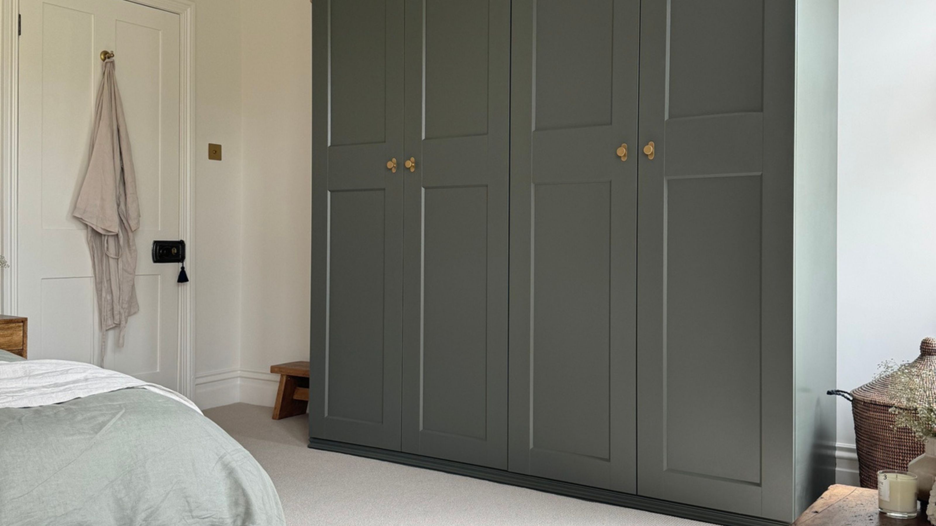Image of a sage green wardrobe in a white room with off-white carpeting, a blue rug, and a bed with sage green bedding.