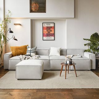 neutral colour living room with wooden floor, light grey sofa with matching footstool and grey rug, with plants either side of the sofa