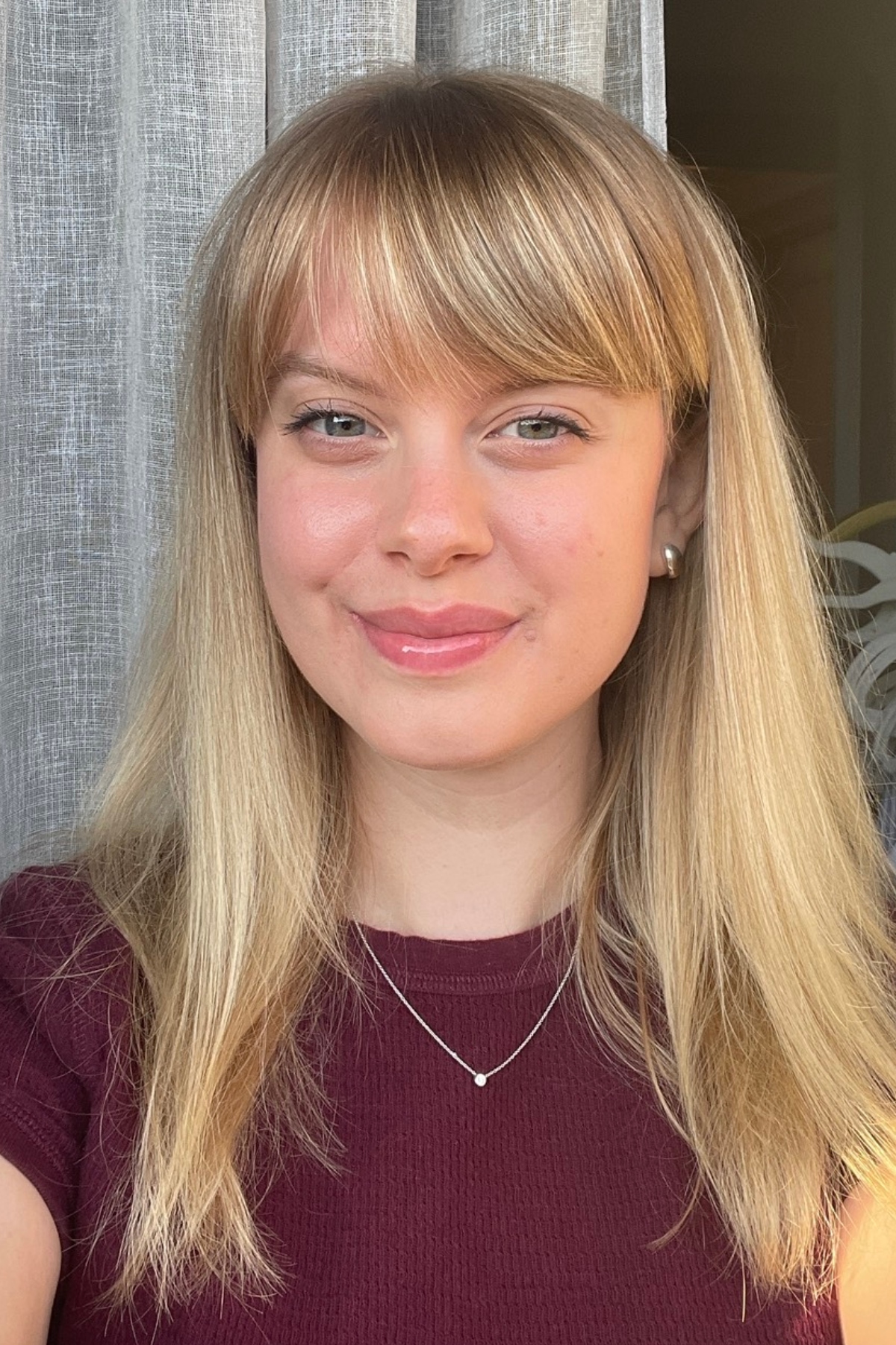 a white woman with blonde hair and bangs in a red short sleeve sweater and gold necklace