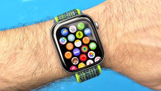 Close-up of the Apple Watch 11 on a user's wrist against a blue background with the app icon grid displayed on the screen