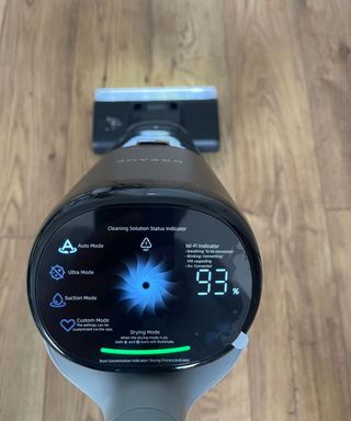 Above shot of Dreame H14 Pro vacuum's display screen showing four cleaning modes, 93% remaining battery, drying mode and cleaning solution status indicator, against wooden floor in Dan's home