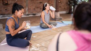 Group of women eating after a workout, sitting on yoga mats together