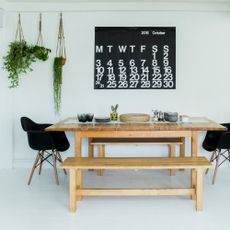 white dining room with bench seating, two Eames style chairs, calendar wall hanging, plants 