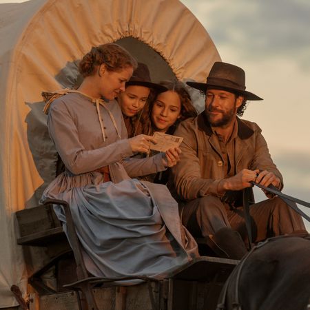 A still from Netflix's 'Little House on the Prairie.' A family (l-r Crosby Fitzgerald as Caroline, Alice Halsey as Laura Ingalls, Skywalker Hughes as Mary, Luke Bracey as Charles) sits on a covered wagon reading a letter