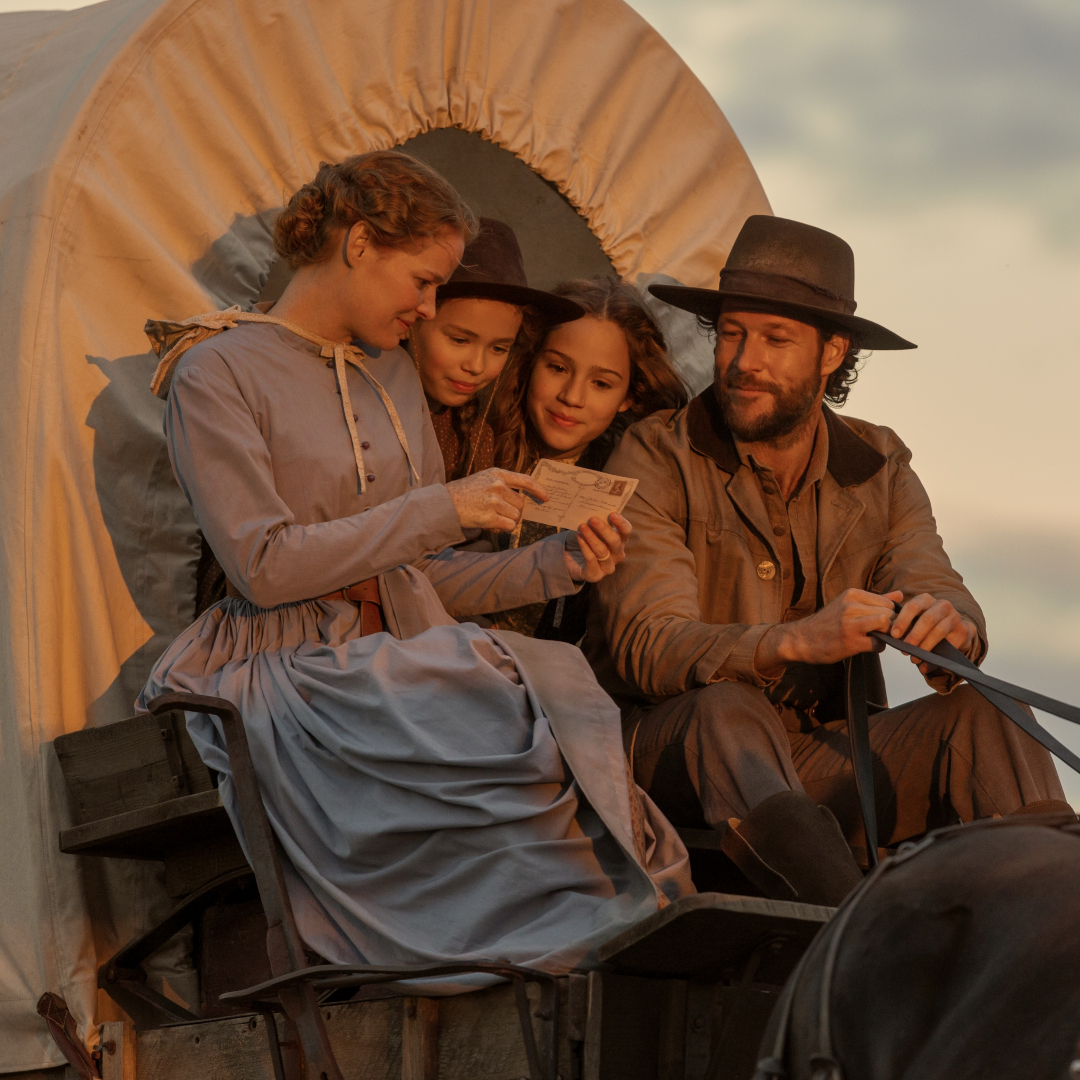 A still from Netflix's 'Little House on the Prairie.' A family (l-r Crosby Fitzgerald as Caroline, Alice Halsey as Laura Ingalls, Skywalker Hughes as Mary, Luke Bracey as Charles) sits on a covered wagon reading a letter