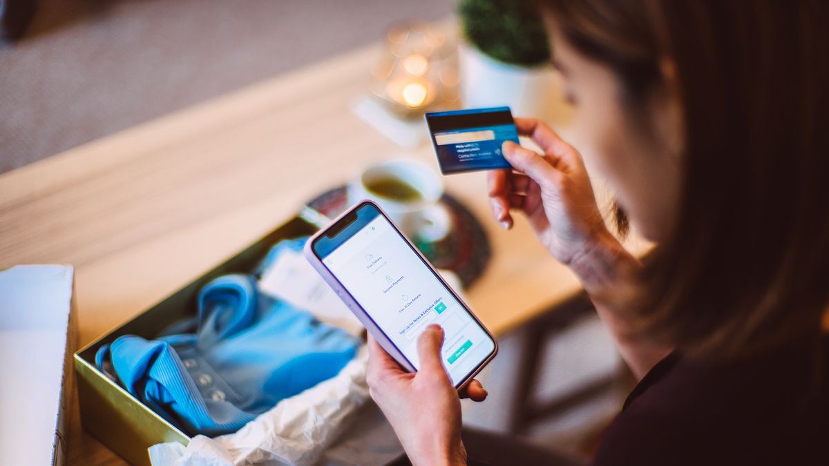 A woman holding a credit or debit card in one hand and carrying out an online purchase on her phone with the other.