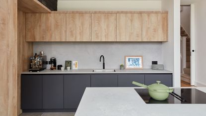 A modern kitchen with wood upper cabinets, dark blue lower cabinets, and concrete countertops